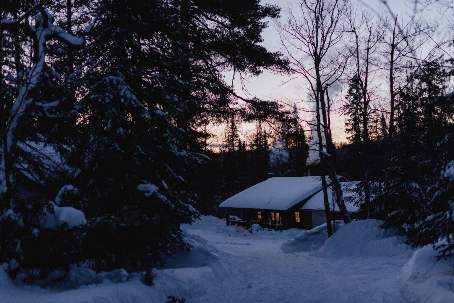 Snow-covered cabin in winter forest at dusk for Coldwater Foundation website 2025.