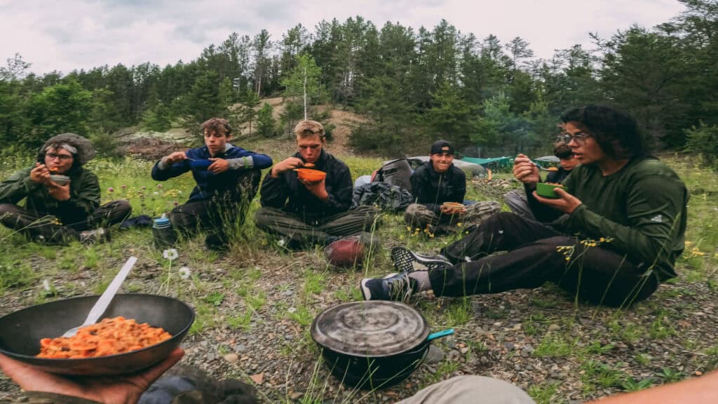 Kids eating outdoors in a green forest setting, promoting youth outdoor programs at Coldwater Foundation.